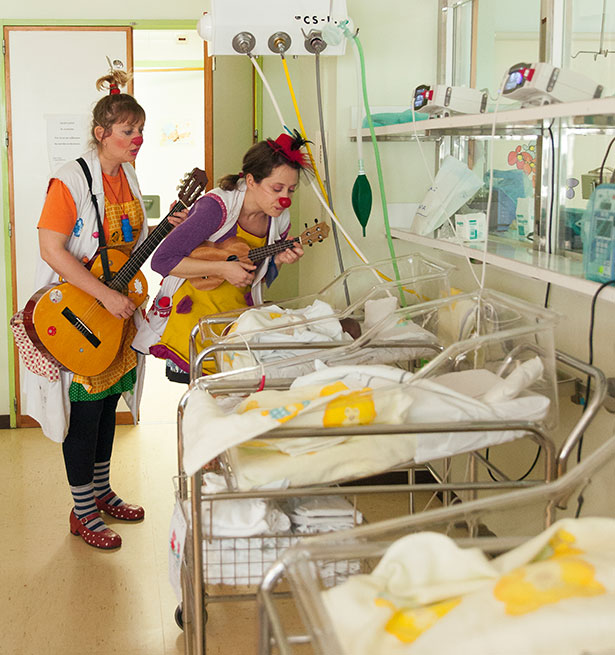 Pareja de payasas de hospital tocando la guitarra y el ukelele y cantándoles a los recién nacidos